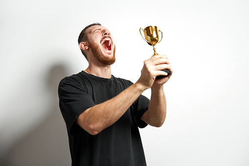 Happy young male or businessman holding his gold trophy and celebrating victory. Studio shot of man with cup as winner. Concept of win, success, human emotions, celebration, achievement, leadership