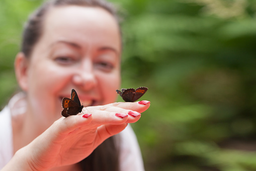 Portrait of an adult happy brunette woman holding butterflies in her hand in a forest clearing and showing psychological appeasement