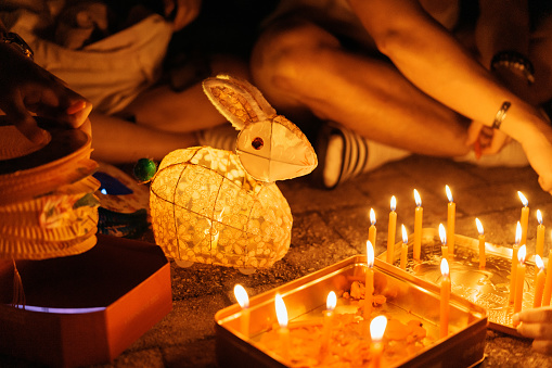 A view of a the traditional objects or items used in the celebration of Chinese Mid-Autumn Festival, including traditional Chinese paper lanterns and ignited slim candles and burned wax inside metal tin trays or boxes, during night time, showing the fun and collective practice or activity to celebrate the Mid-Autumn Festival. A photo showing the Chinese culture of Mid-Autumn Festival where people celebrate the unity and togetherness of families and friends.