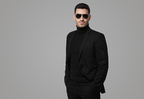 Serious body guard or secret agent wearing suit and sunglasses, isolated on grey background