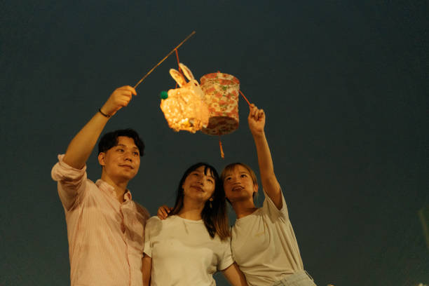 young asian friends holding traditional paper lantern while celebrating chinese mid-autumn festival outdoors at night together - midautumn festival 個照片及圖片檔