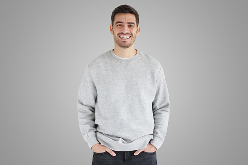 Daylight portrait of young laughing handsome man, wearing oversized sweatshirt, isolated on gray background