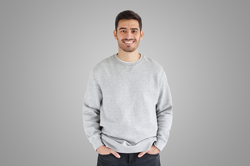 Daylight portrait of young handsome man, wearing oversized sweatshirt, isolated on gray background