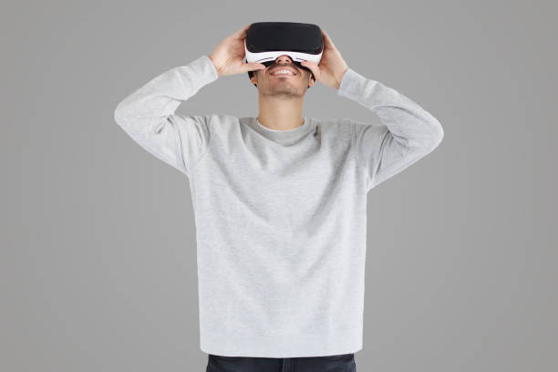 istock Smiling man holding virtual reality goggles with both hands on gray background 1430990290
