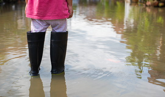 A child with black boots walks on a flooded road.