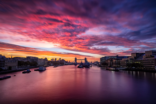 Colorful sunrise behind the skyline of London, England, with Tower Bridge and reflections in the river Thames