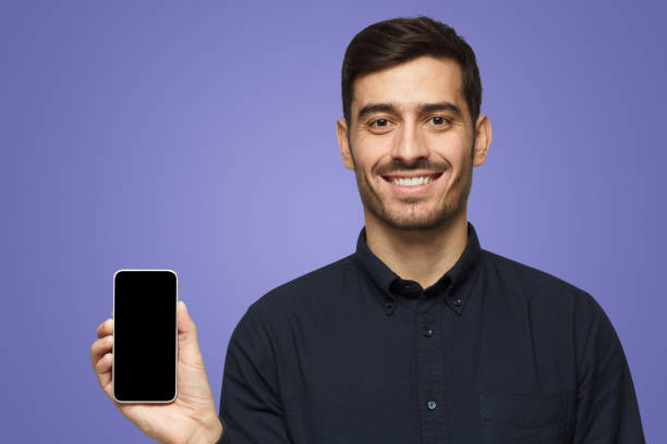 istock Smiling business man holding blank smartphone with empty black sreen in hand on purple 1430993110