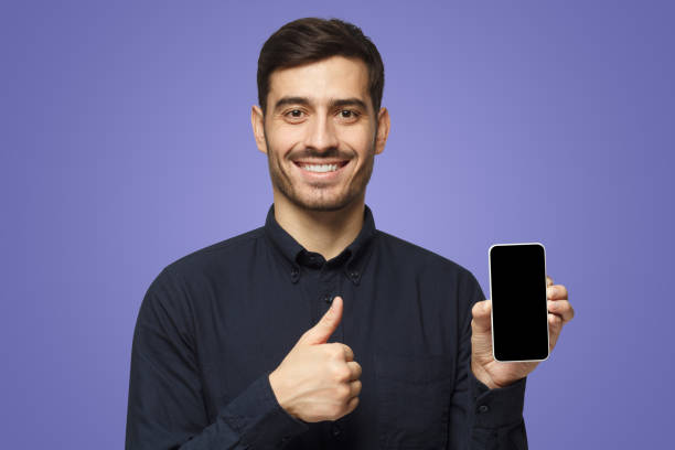 istock Young man holding blank smartphone, smiling at camera, showing thubms up gesture 1430993202