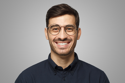 Portrait of bearded young man with hair bun wearing white t-shirt. Confused male student looking at camera. Studio shot, grey background.