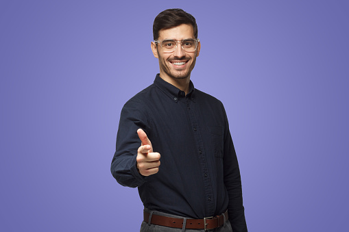 Portrait of young man pointing at camera as if choosing viewer for his project, isolated on purple background