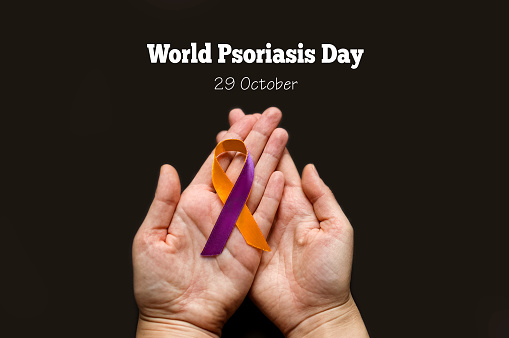 World Psoriasis Day. Woman's hands are holding a purple-orange ribbon on a black background. Treatment of skin diseases, dermatitis, eczema, psoriasis. Medical banner