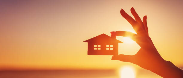 istock Woman's hand holding a model of a house on sunset evening 1430996928