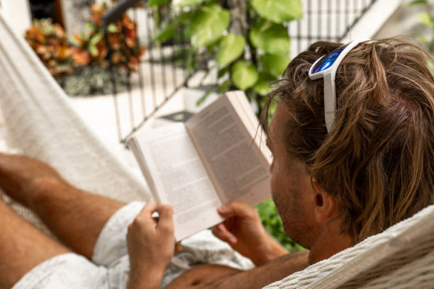 istock Young man relaxing in an hammock reading a book, tropical climate 1430997378