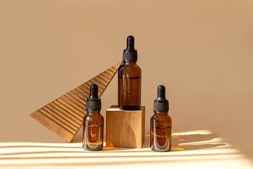 istock Set of amber glass bottles with dropper lid on a 3d wooden podium in the sunlight. Containers with serum for face close-up on brown background 1430997435