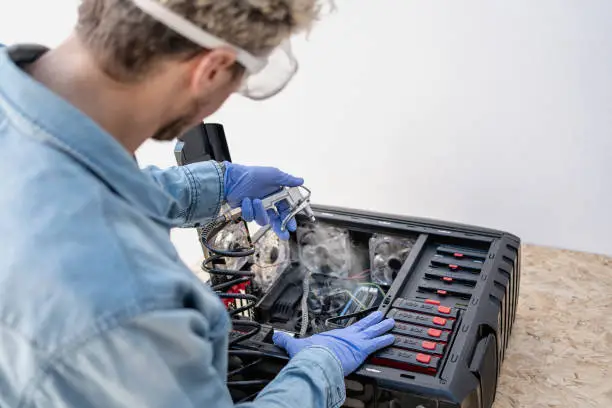 Man with protective glasses ang gloves using compressed air gun for blowing inside of computer. Close up. Copy space