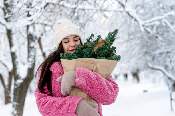 A beautiful dark-haired young woman in a pink faux fur coat with fir branches in her hands in a winter park.New Year,Christmas and eco-friendly concept stock photo