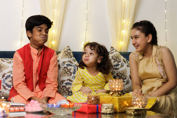 Kids, brother sister friends siblings dressed up in ethnic wear smiling enjoying togetherness with gift box celebrating diwali Hindu festival Laxmi poojan with ambient light bokeh stock photo