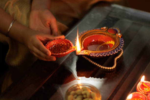 Close up of Young girl lighting Handcrafted Eco Friendly Clay Diya Deep Dia with ambient light bokeh for Hindu festival Laxmi poojan (Diwali) stock photo