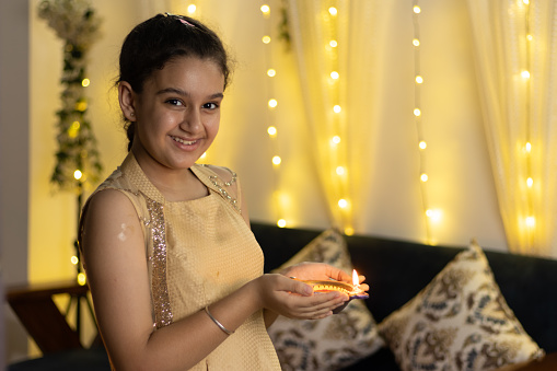 young girl looking at camera holding Handcrafted Eco Friendly Clay Diya Deep Dia with ambient light bokeh for Hindu festival Laxmi poojan (Diwali)
