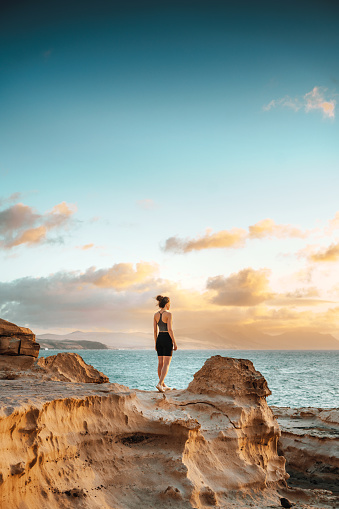 Woman standing on a cliff overlooking an ocean and spectacular sunset