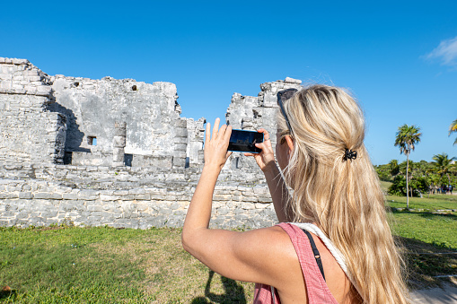 Female tourist takes photos using mobile phone, Mayan ruins in Tulum, Mexico