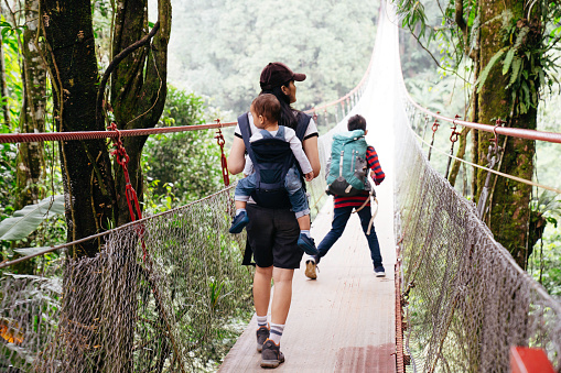 asian woman walking with her sons on the bridge during hiking in the forest