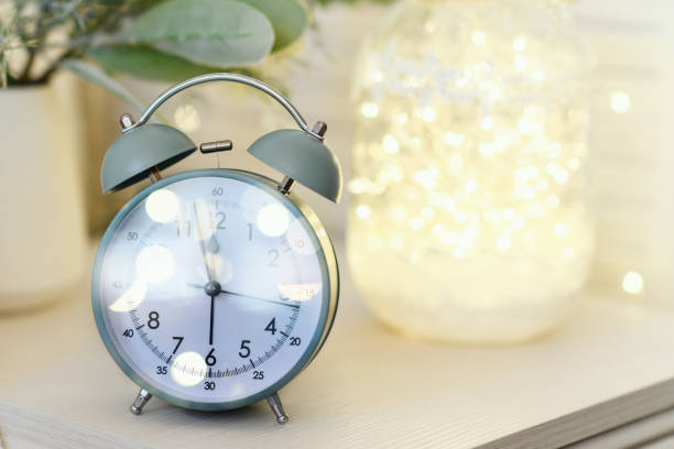 istock Alarm clock standing on nightstand near bed with small christmas tree and light lamp with garland. Christmas, New year concept. 1431022122