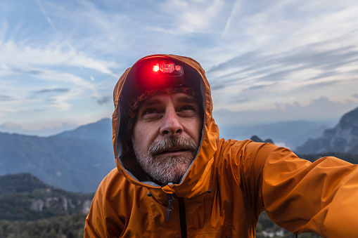 Hiker with rain jacket and headlamp looking up sky in the mountains