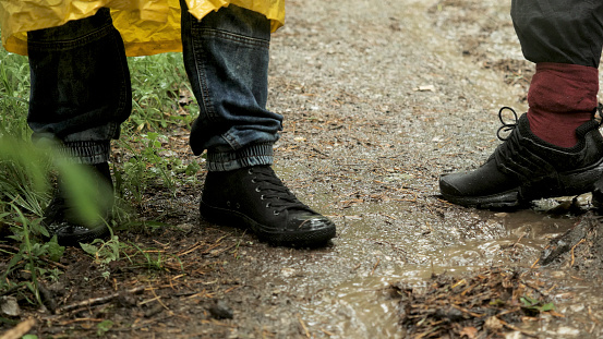 People trekking in the forest under the rain. Close up of male legs standing on the wet forest ground with falling rain drops.