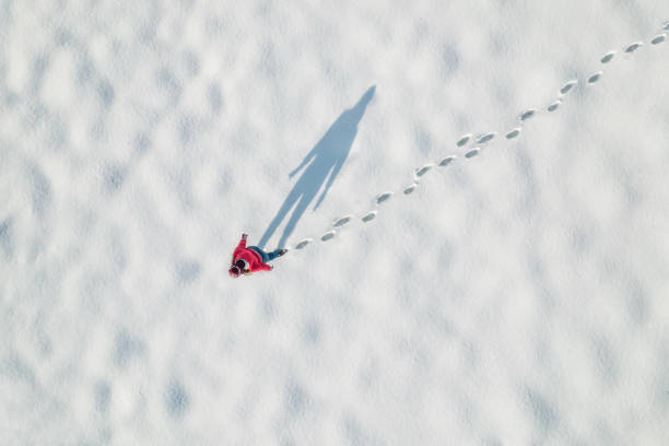 Woman in a red christmas jacket walking on the snow and doing footprints in a park. Winter. Drone, top, aerial view. stock photo