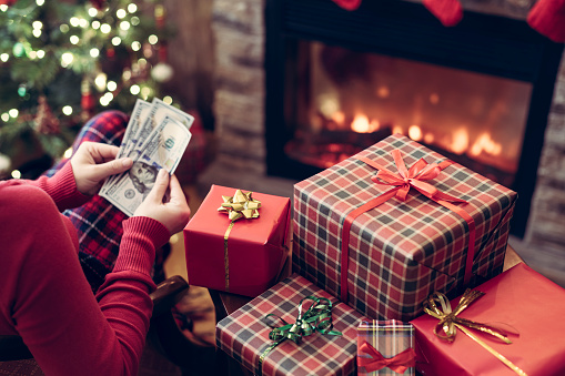 Woman counting american dollars planning sitting near christmas tree and fireplace and packing gift box. Spending money at christmas time. oncept.