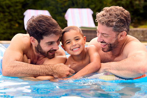 Same Sex Family With Two Dads And Son On Holiday In Swimming Pool Together