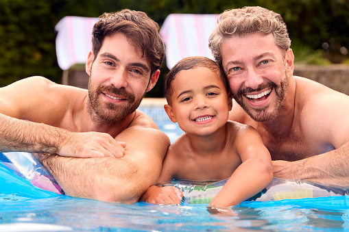 Portrait Of Same Sex Family With Two Dads And Son On Holiday In Swimming Pool Together