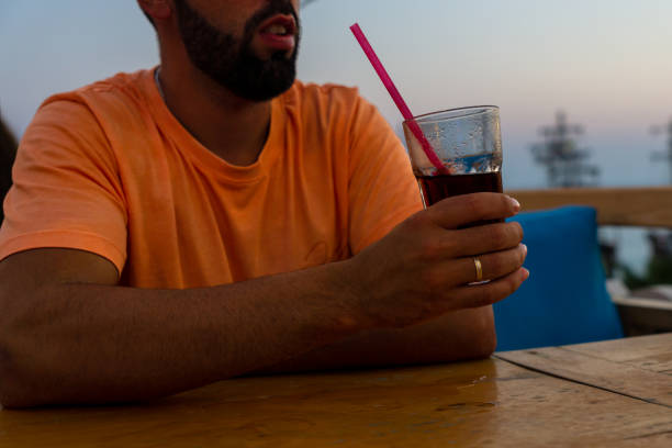 istock Man sitting at a bar table at sunset while drinking a soft drink from a glass with a straw and having a good time. 1431034179