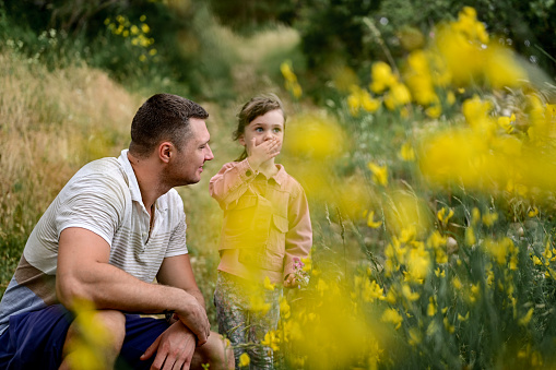 Father explaining plant to daughter while walking in a forest together. Parent explain to his child about nature and wild flowers in a forest outdoors. Man telling story to a daughter while hiking throw the forest.