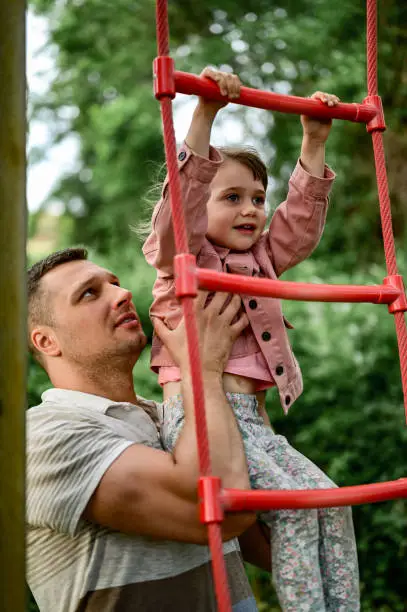 Healthy happy childhood. climbing monkey bars at playground. Active little girl climbing monkey bar outdoors with help and support of her loving father. happy time together. father and kid. fathers day.