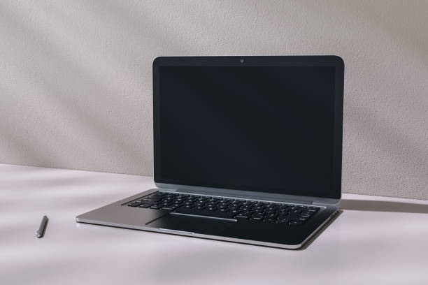 istock Perspective view on modern laptop blank dark screen with place for your logo or text on glossy table with pen and shadows on light wall background. 3D rendering, mock up 1431035602