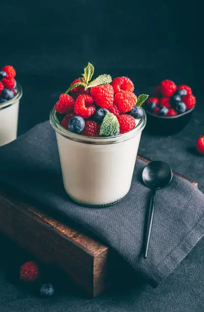 Photo of Homemade italian dessert panna cotta with fresh raspberry, blueberries and mint in jar on black background