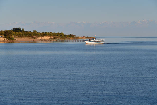 Lake Issyk-Kul, white ship and high snow covered mountain peaks Tien Shan on opposite shore, Kyrgyzstan