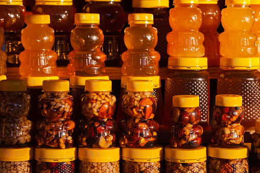 Assortment of honey with nuts in bear shaped plastic jars stand on a shop window in a row. Close up photo with selective soft focus