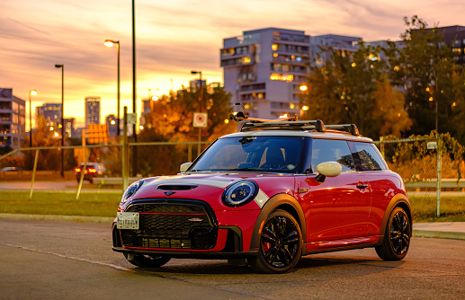 Toronto, Ontario, Canada- October 5, 2022. Evening image of Chili red colour MINI COOPER on the streets of Toronto East side, Canada. This is the third generation model F56 JCW, since BMW took over iconic brand of MINI. MINI featured in the photo is John Cooper Works model, the most powerful 2 door version. For the first time, this compact car features engine build and designed by BMW, and packs even more power and torque than previous models since 2002 to present. Original design clues and themes are still present on this brand new model. Mini has been around since 1959 and has been owned and issued by various car manufacturers.