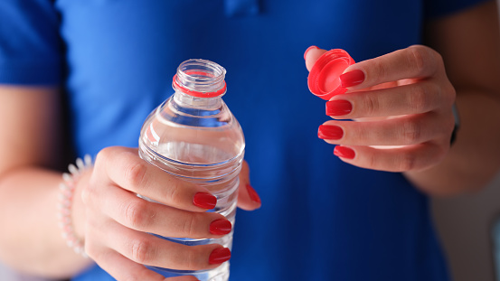 Woman opening plastic bottle with clean water. Water benefits for skin and health