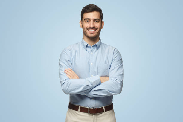 uomo d'affari moderno in camicia blu casual in piedi con le braccia incrociate su sfondo blu - crossing human arm leadership men foto e immagini stock