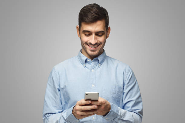 istock Smiling business man in blue shirt reading sms, using smartphone, isolated on gray background 1431057950