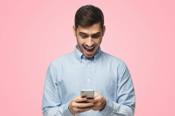 istock Young businessman looking at phone with surprise expression, isolated on pink background 1431057952
