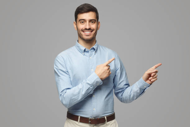 istock Smiling businessman pointing right with two hands looking at camera, isolated on gray 1431057953