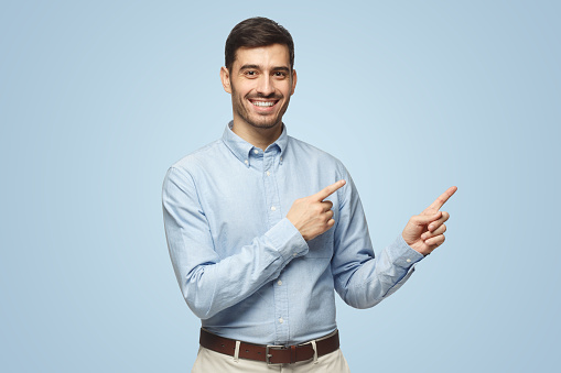 Happy smiling young business man pointing away, isolated on blue background