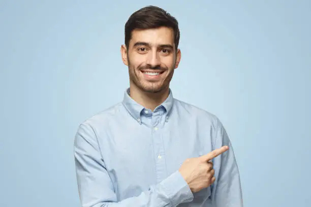 Photo of Smiling business man pointing right with index finger looking at camera on blue background