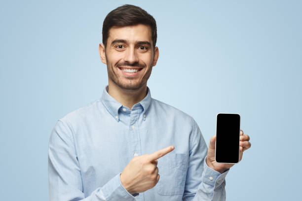 istock Handsome smiling man holding and showing with finger blank smartphone with copyspace for ads of app 1431057988
