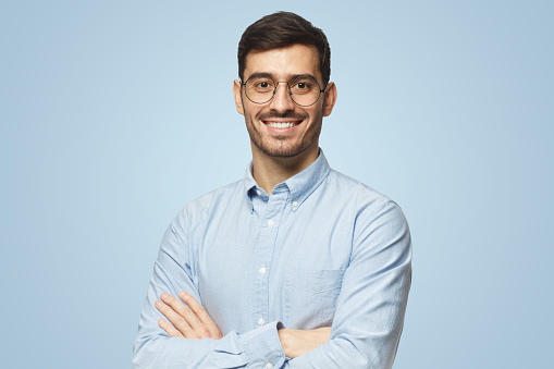 Modern businessman in blue shirt standing with crossed arms, isolated on blue background